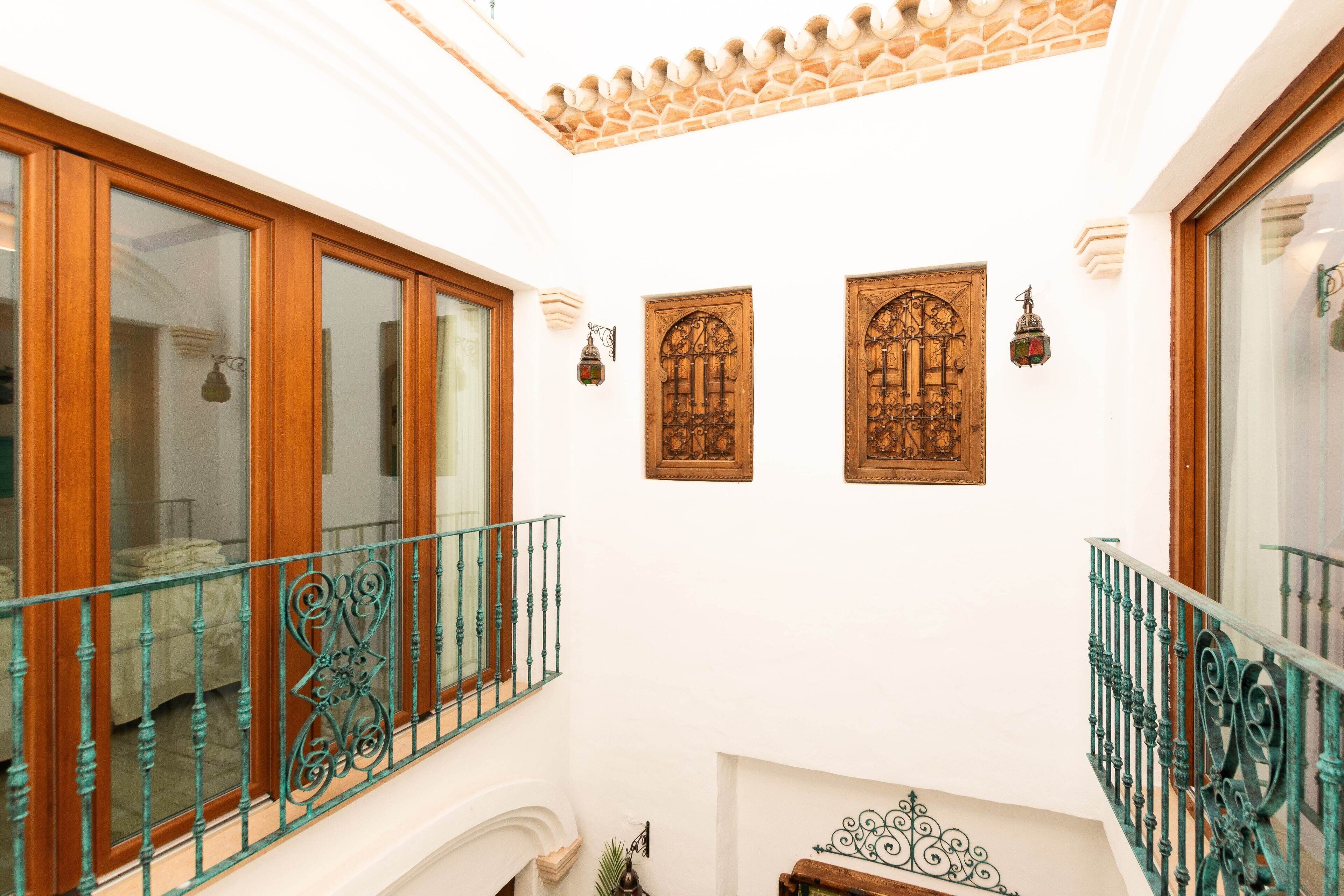 A hotel interior with a balcony, wooden doors, and decorative wall sconces.