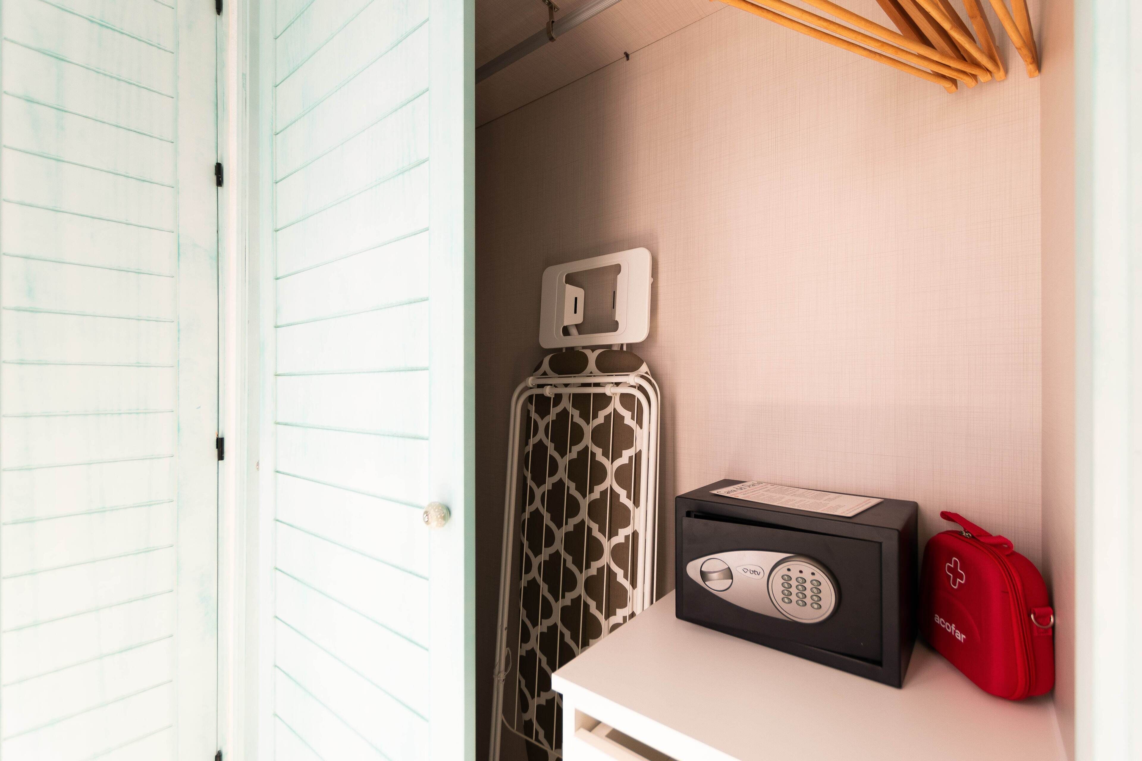 Una habitación de hotel con una puerta blanca, un radiador, un dispositivo electrónico negro y un bolso rojo.