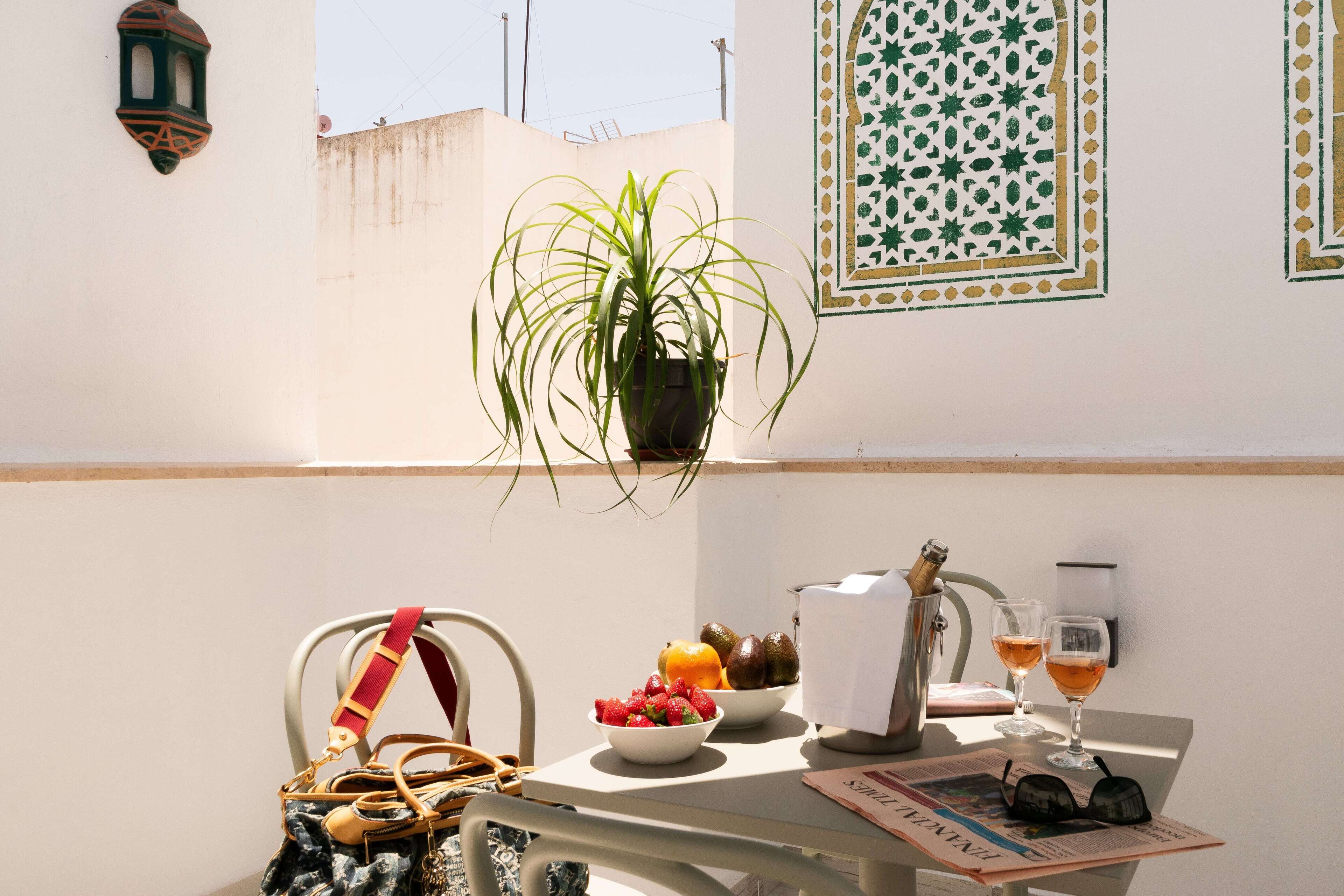 A balcony with a potted plant, fruit bowl, wine glasses, and a handbag.