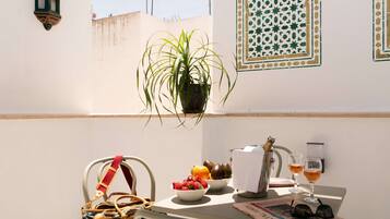 A balcony with a potted plant, fruit bowl, wine glasses, and a handbag.