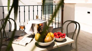 A table with a newspaper, a bowl of fruit, a glass of wine, and a bottle of water on a balcony.
