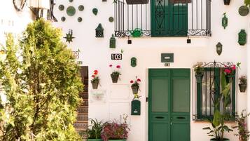 A white building with green shutters and balconies, adorned with potted plants and flowers.