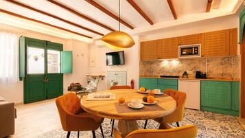 A dining area with a wooden table and orange chairs, a kitchen with green cabinets and a microwave, and a television above the counter.