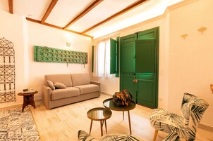 A living room with a sofa, a small table, a chair, a green door, and a decorative wall piece.