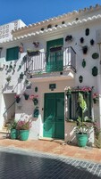 Un edificio blanco con contraventanas verdes, números 103 y 102, balcones con plantas en macetas y una entrada con mosaicos.