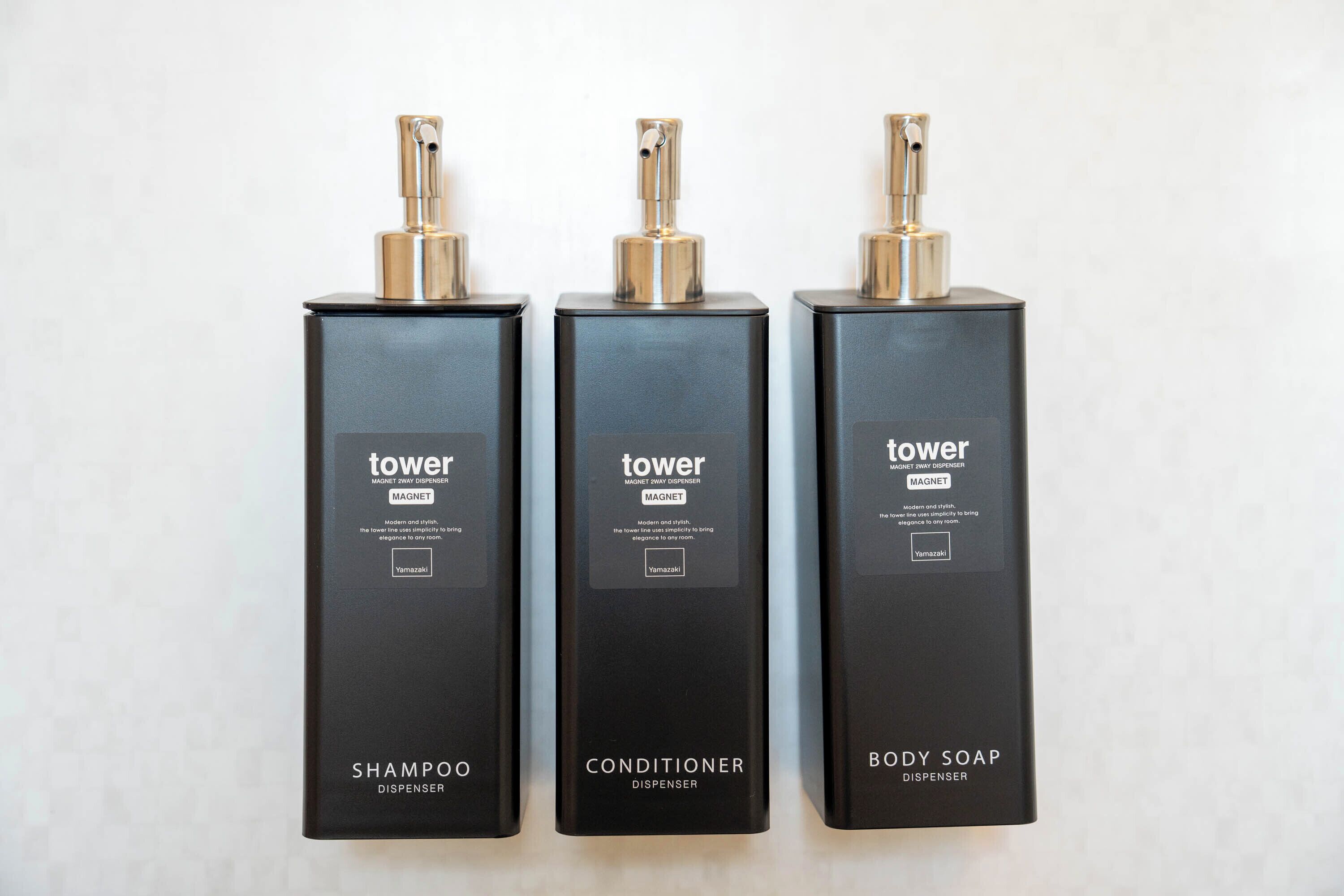 Three black dispensers labeled 'tower' for shampoo, conditioner, and body soap.