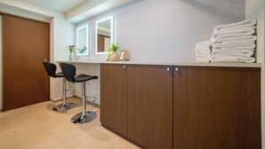 Ein Badezimmer mit Waschtisch aus Holz, zwei schwarzen Barhocker, einem Spiegel und einem Stapel Handtücher.