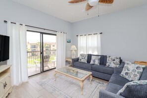 Sala de estar com sofá, mesa de centro de vidro, televisão e varanda com vista.