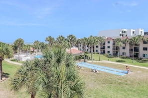 A hotel with a pool, palm trees, and a clear view of the ocean.
