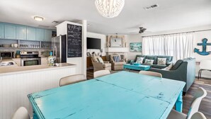 Una cocina moderna con una isla central, un comedor con mesa azul y una sala de estar con sofá y una gran decoración de ancla.