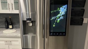 Un réfrigérateur en acier inoxydable doté d’un écran numérique, d’un distributeur d’eau et d’une bouteille de vin posée sur le plan de travail.