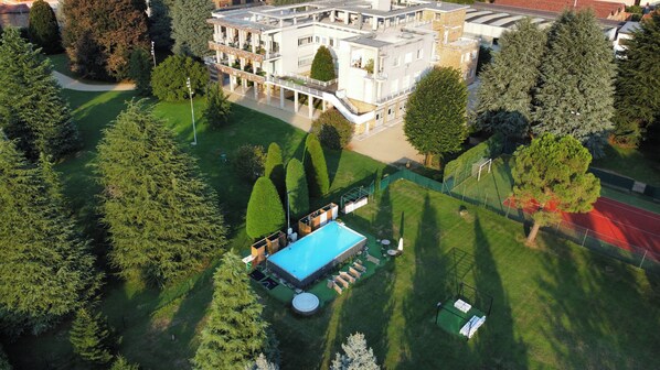 Vue aérienne d’un hôtel doté d’une piscine, d’un court de tennis et d’un jardin aménagé.