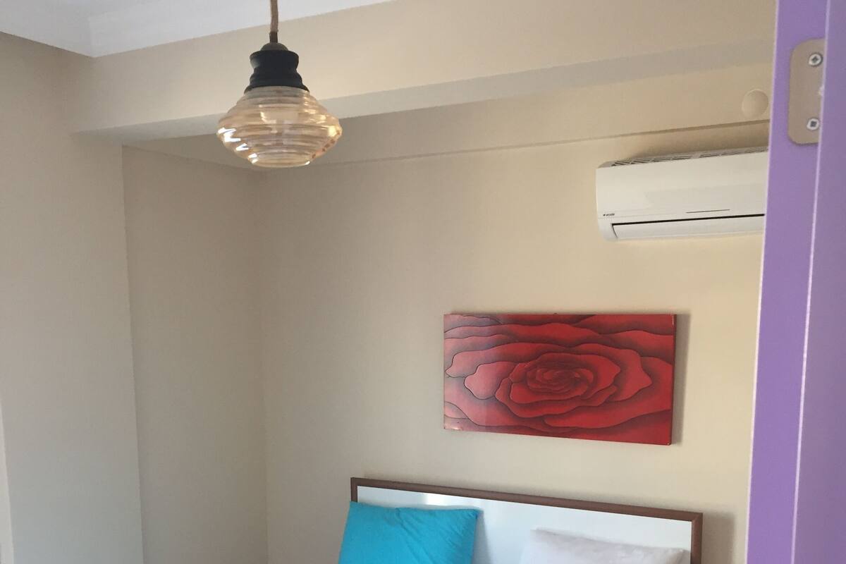 A neatly made bed with blue and white bedding, a red rose artwork on the wall, and a hanging light fixture.