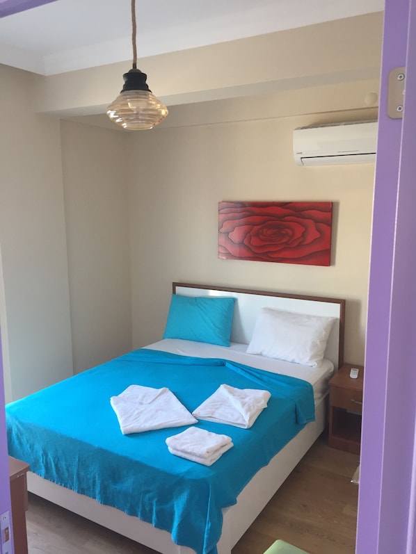 A neatly made bed with blue and white bedding, a red rose painting on the wall, and a hanging light fixture.