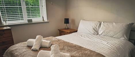Un dormitorio con cama, cómoda de madera, mesita de noche y ventana con persianas.