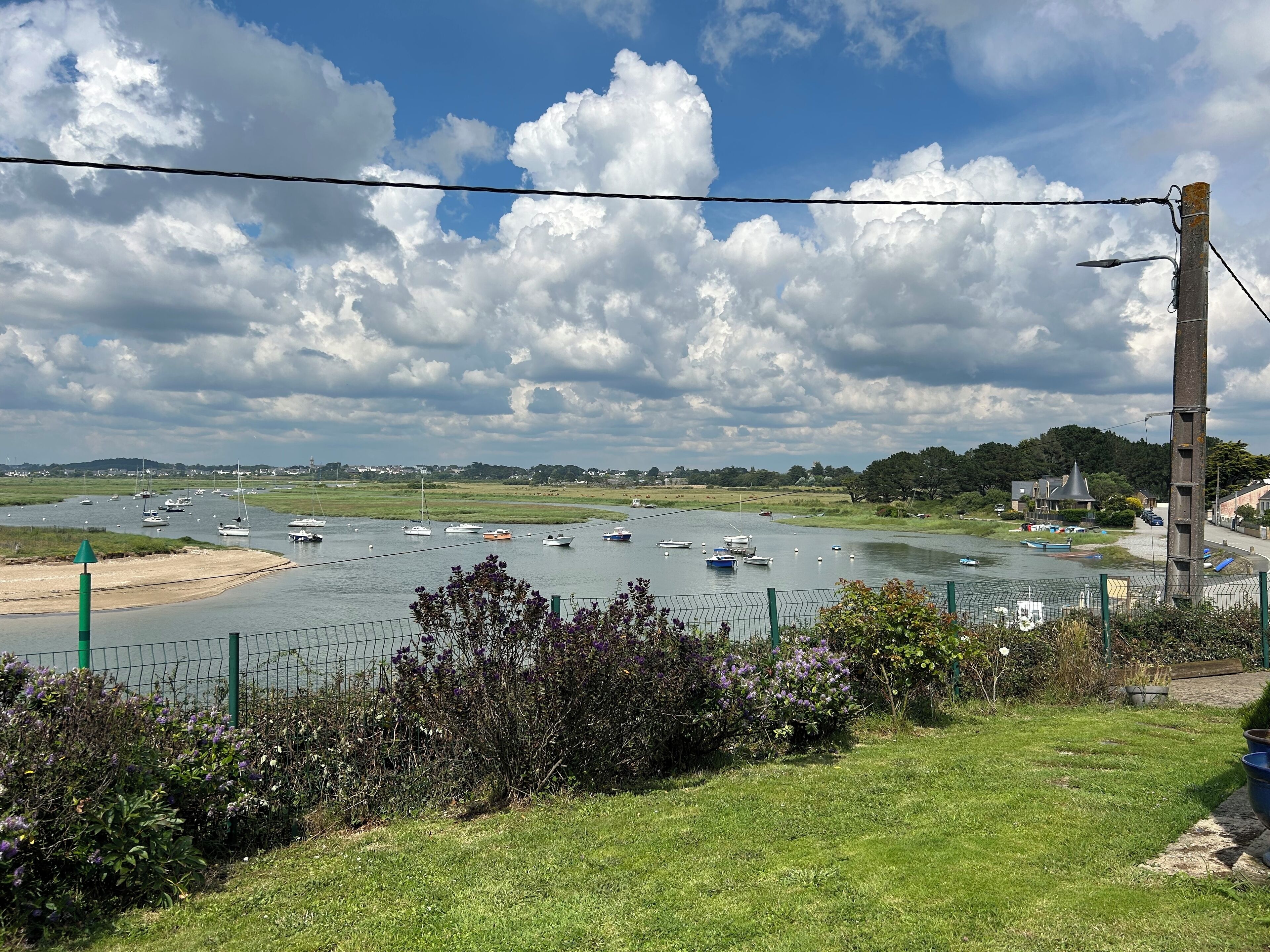 A riverside view with boats, greenery, and a fence.