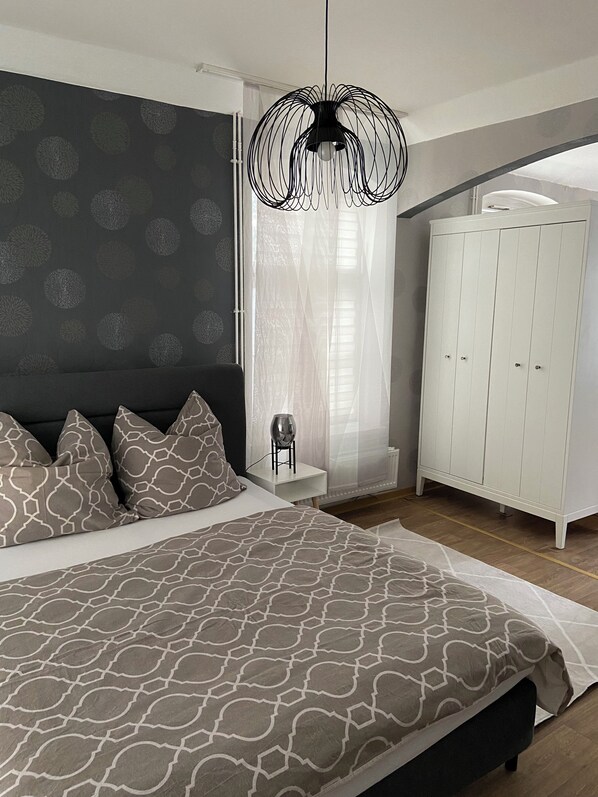Ein Schlafzimmer mit einem großen Bett, einem weißen Kleiderschrank und einer außergewöhnlichen schwarzen Pendelleuchte.