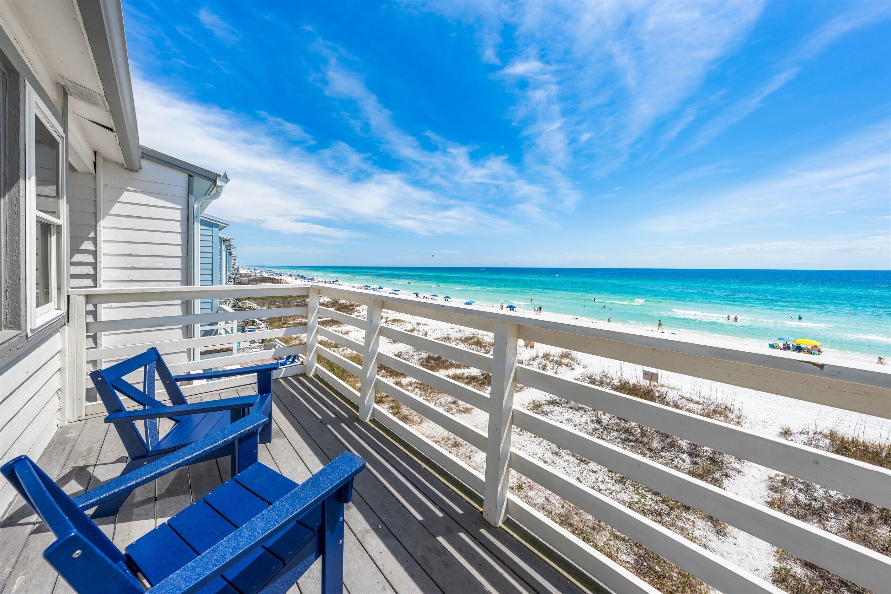 A balcony with blue chairs overlooking a beach with white sand and turquoise water.