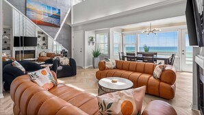 A spacious living area with a large sofa set, a flat-screen TV, and a dining area with a view of the ocean. - Seawinds 9 | Renovated Gulf-Front Escape (Mramar Beach)