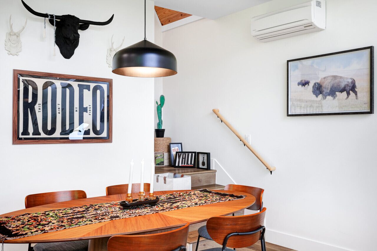 A dining area with a wooden table, chairs, a pendant light, a framed 'RODEO' sign, a cactus, and a framed picture of a bison.