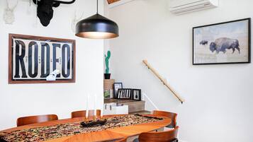 A dining area with a wooden table, chairs, a pendant light, a framed 'RODEO' sign, a cactus, and a framed picture of a bison.
