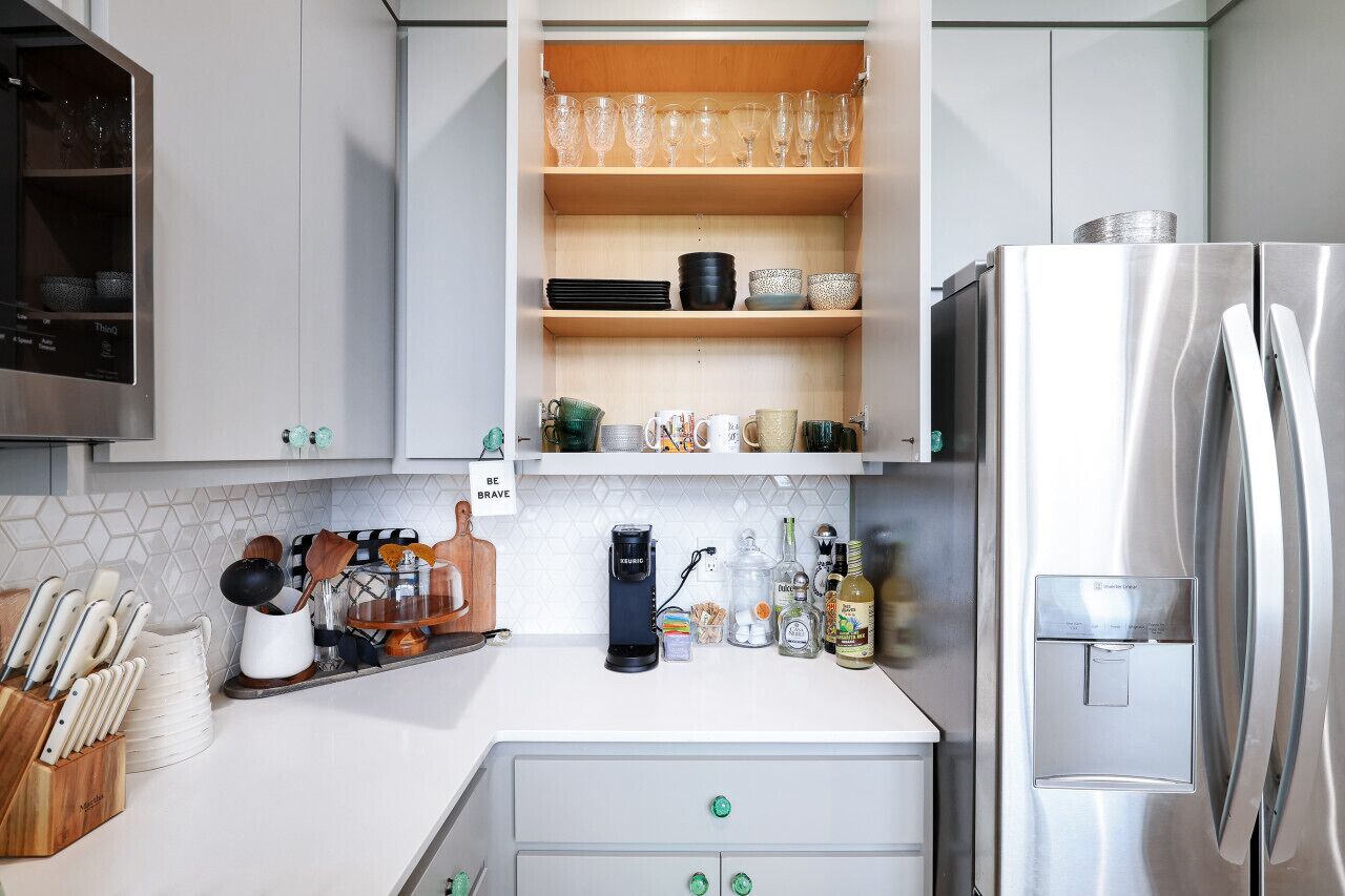 A kitchen with white cabinets, a stainless steel refrigerator, and a built-in shelf with glassware and dishes.