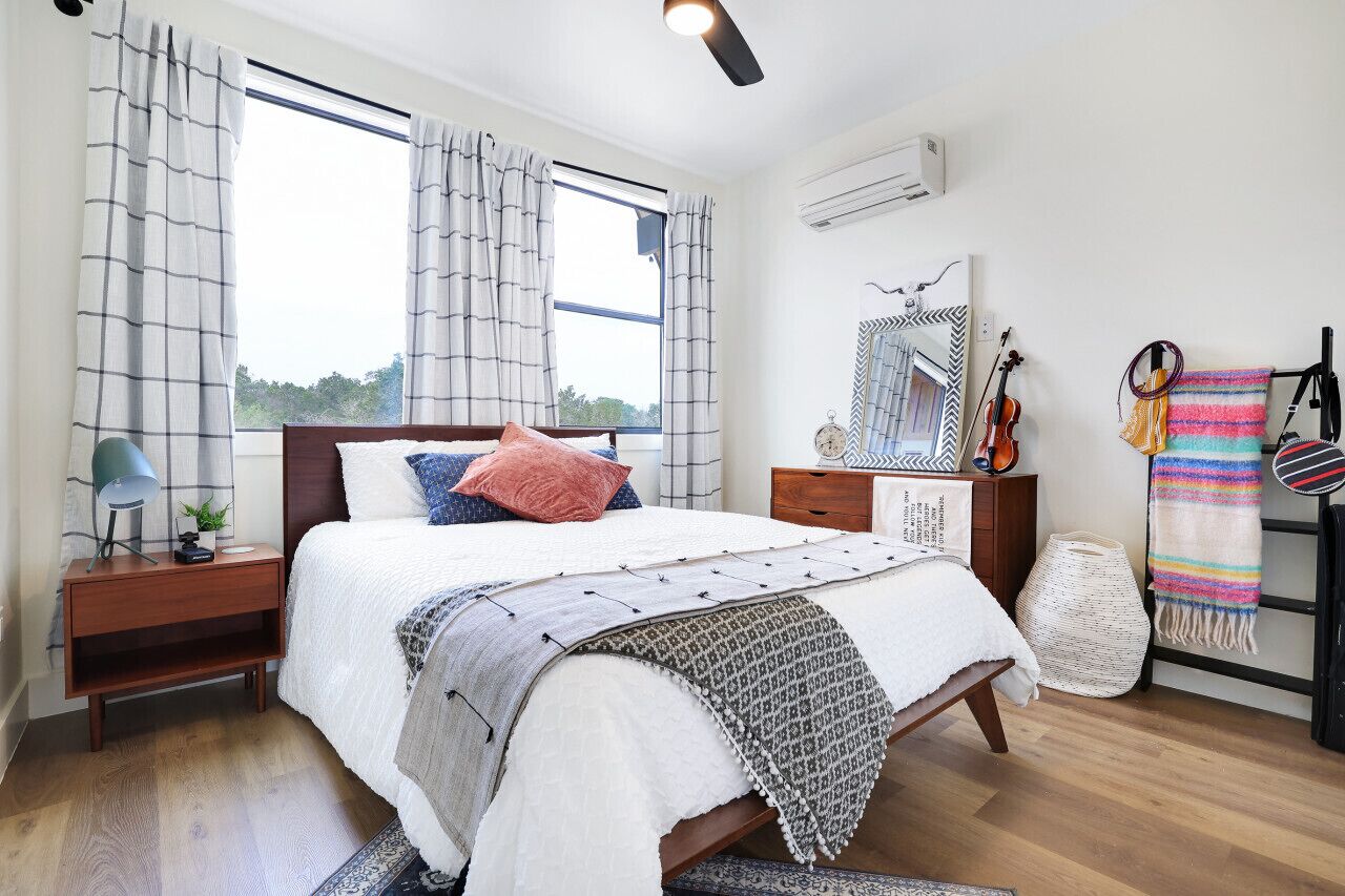 Un dormitorio con cama, mesita de noche y ventana con cortinas.