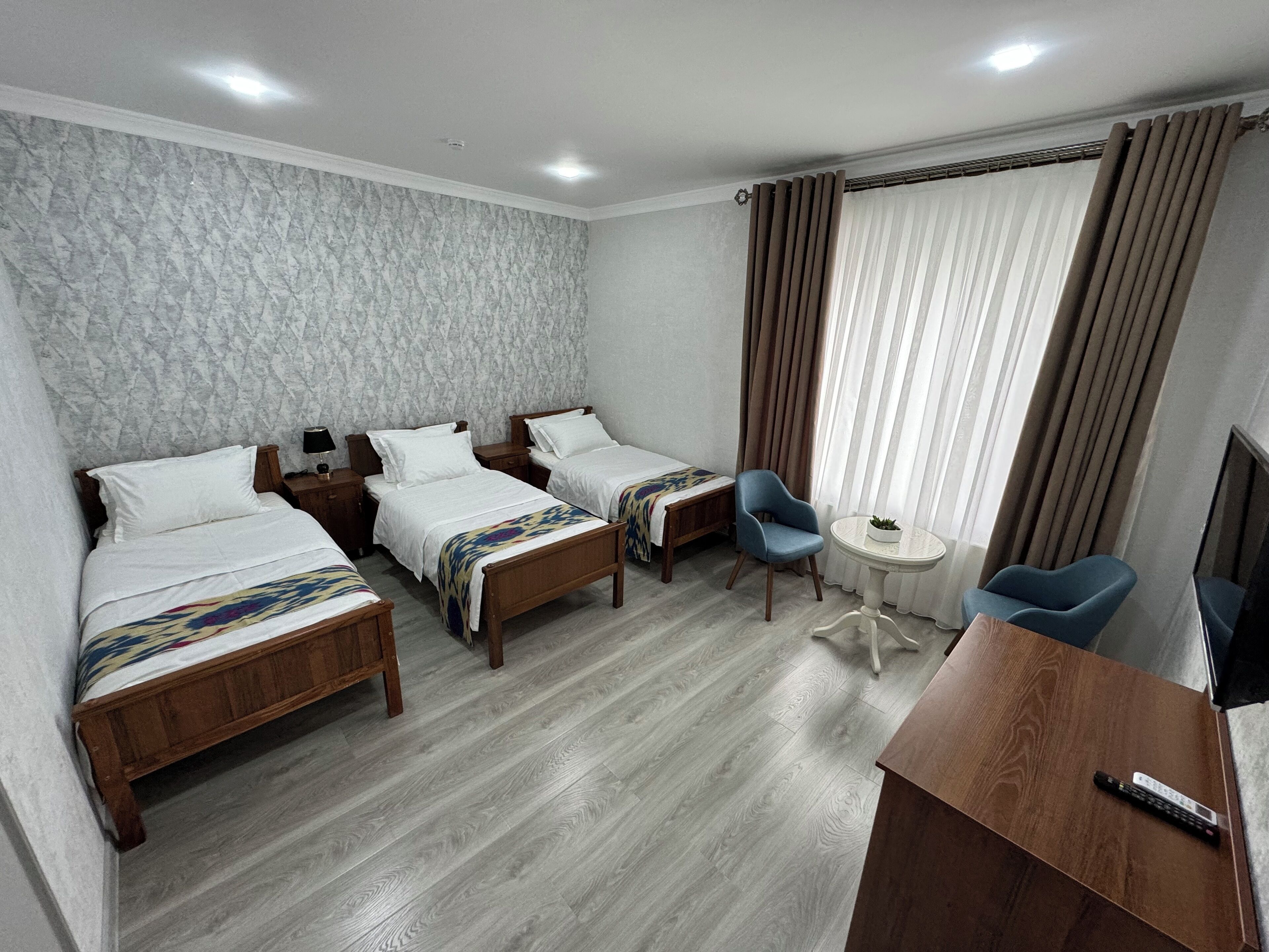 Ein Hotelzimmer mit zwei hölzernen Betten, einem kleinen runden Tisch, einem blauen Stuhl und einem Fernseher auf einem Holzständer.