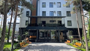A modern hotel with a checkered outdoor area, wooden benches, and a covered entrance. - DSF GARDEN HOTEL (Tashkent)
