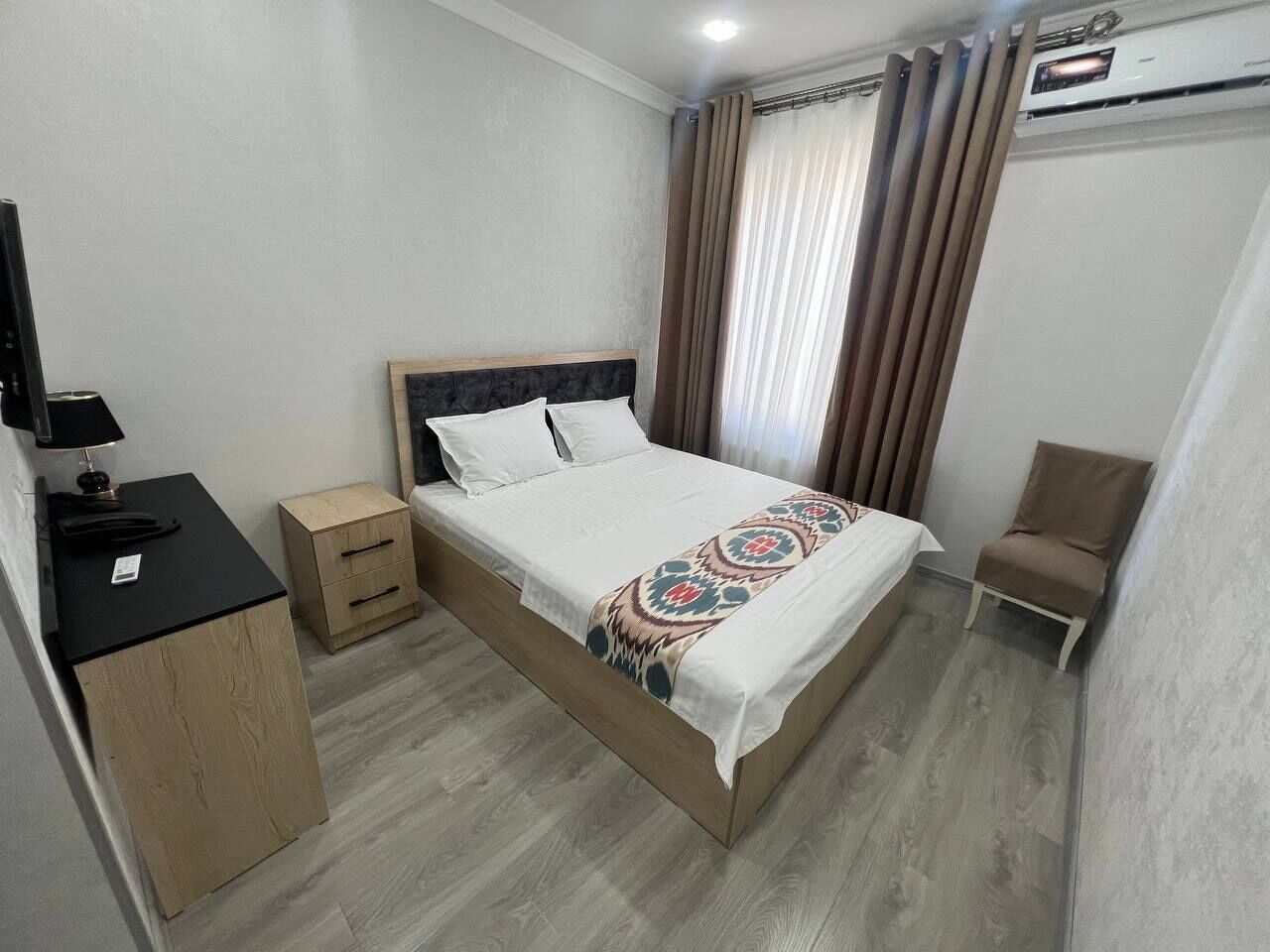 A hotel room with a bed, a desk, a chair, and a small cabinet.