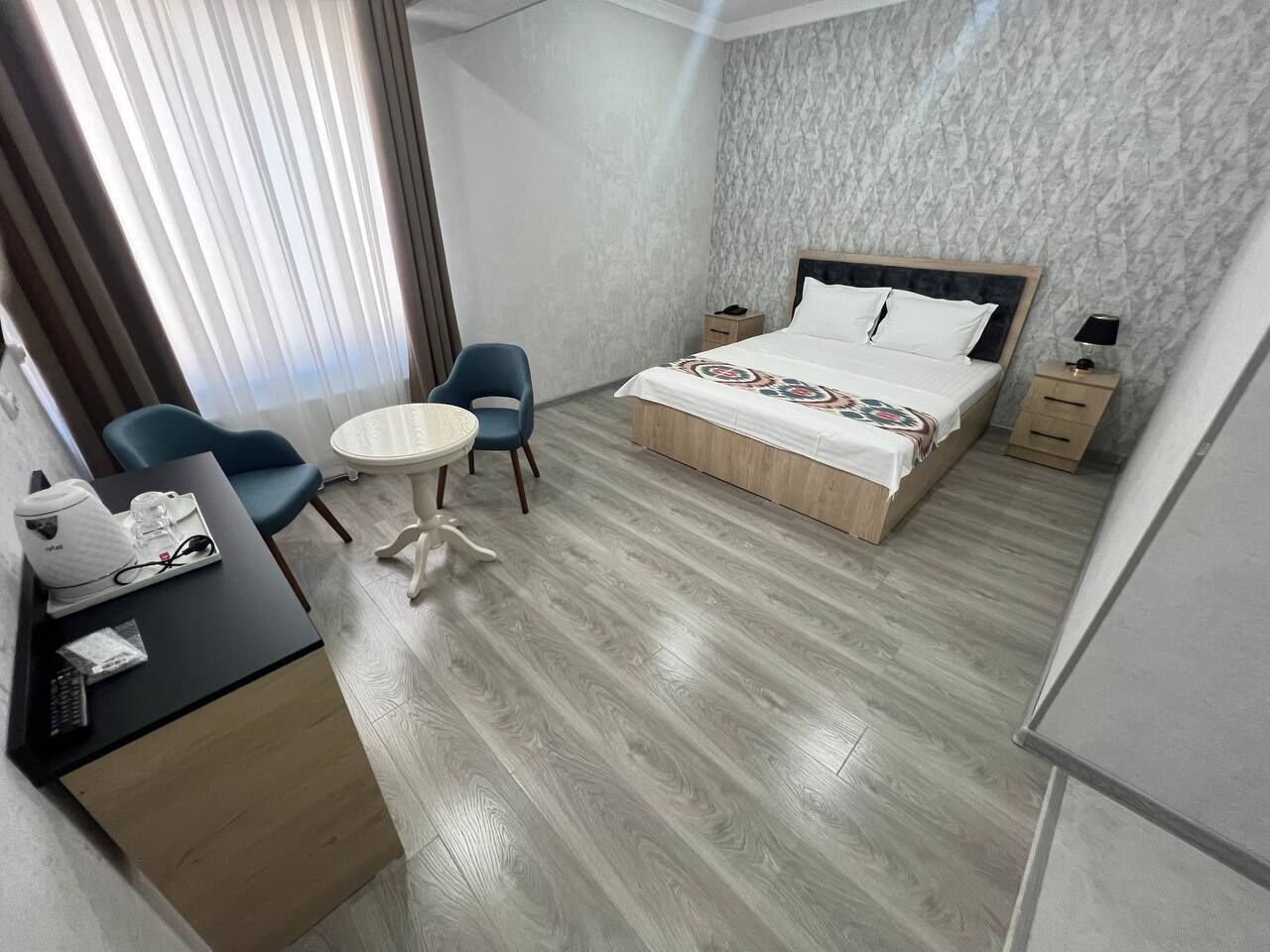 Habitación de hotel con una cama, un escritorio con silla, una mesita pequeña y una mesita de noche.