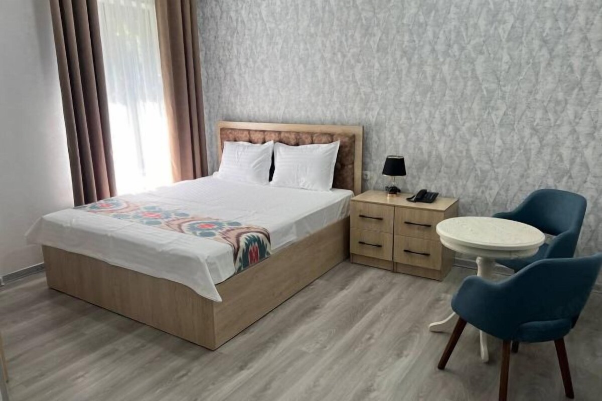 A hotel room with a bed, bedside table, lamp, and two chairs.