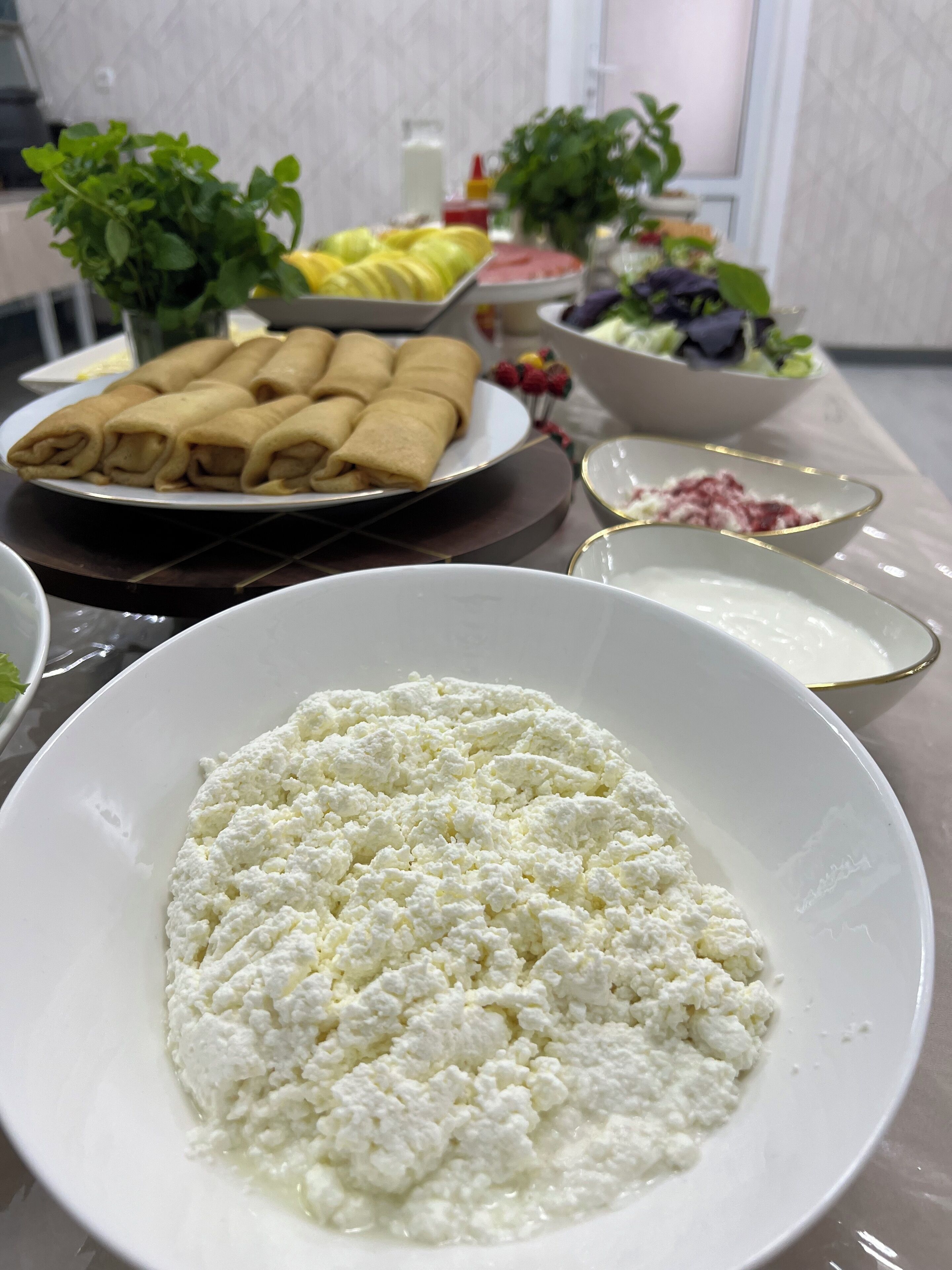 A table with various food items including a bowl of cottage cheese, a plate of rolled pastries, and a bowl of salad.