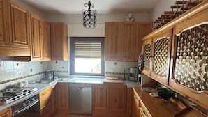 Una cocina con armarios de madera, estufa a gas, lavavajillas y una ventana con persianas.