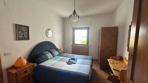 Un dormitorio con cama, mesita de noche, armario de madera, ventana y lámpara colgante.