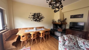 Un comedor con una mesa y sillas de madera, una chimenea, un televisor y un sofá floral.