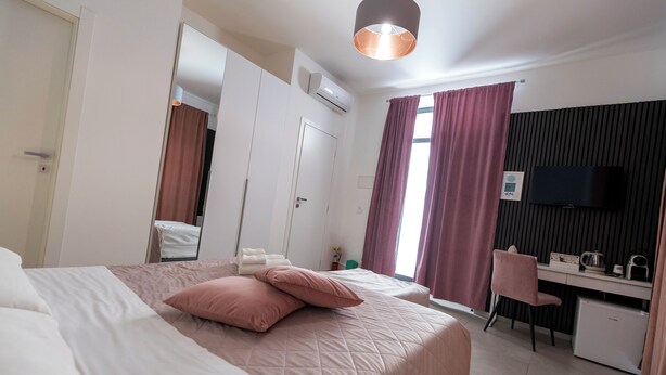 Una habitación de hotel con cama, escritorio, silla, televisor y ventana con cortinas.