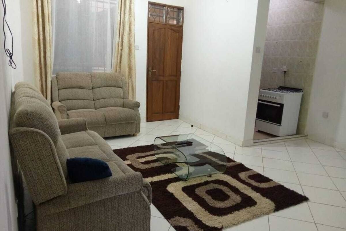A living room with a sofa, a glass coffee table, and a patterned rug.