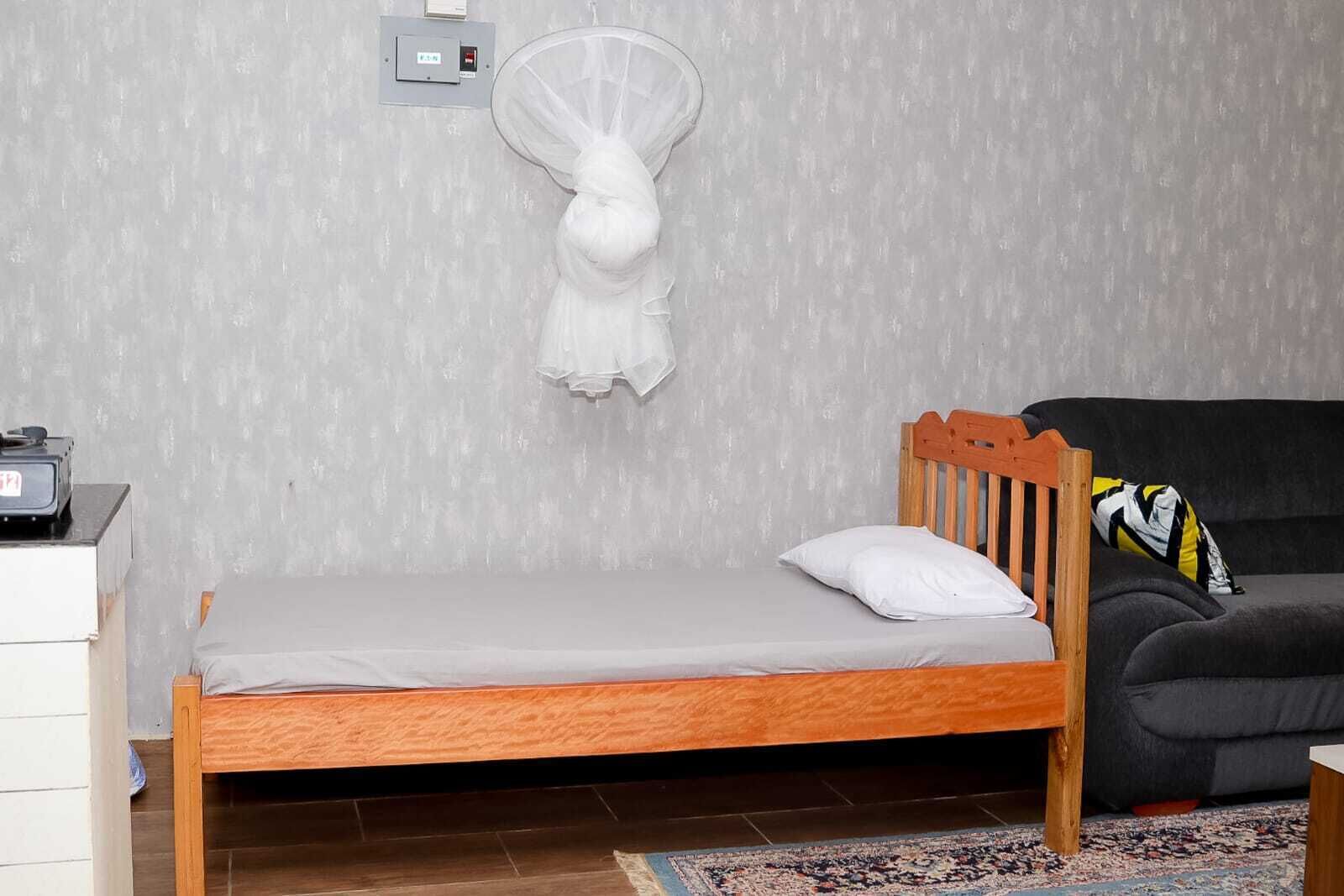 Una habitación pequeña y funcional con una cama individual, cabecera de madera, un sofá oscuro y un tapete estampado.