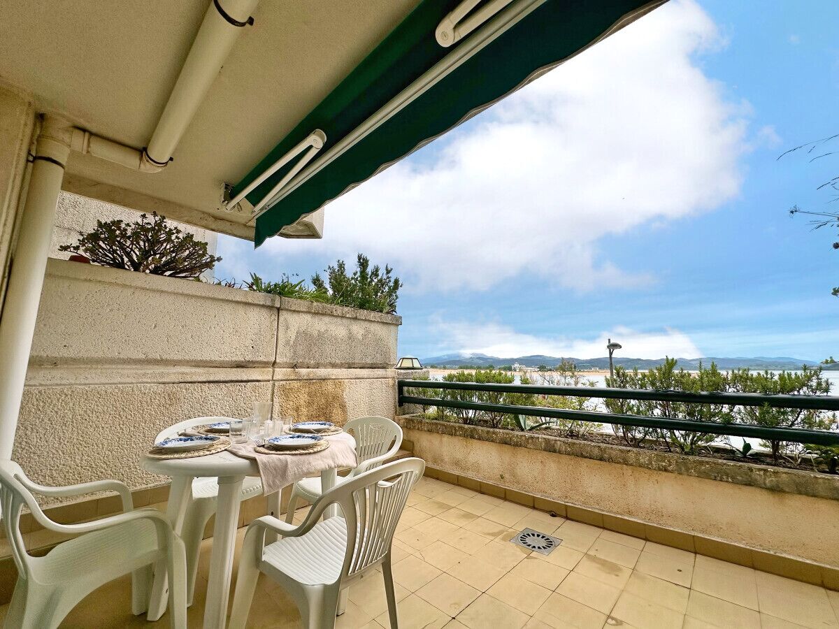 A balcony with a table set for dining, chairs, and a view of the sea and distant landscape.