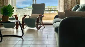 Una sala de estar con vista al cielo y un balcón. Hay dos sillones, un sofá y una mesita con una planta.