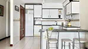 Una cocina moderna con armarios blancos, una isla central con taburetes y un refrigerador.