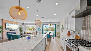 A modern kitchen with a large island, stainless steel appliances, and pendant lighting. - Electric Slide- Lazy River, Pickleball, Resort backyard & Game room (coachella)
