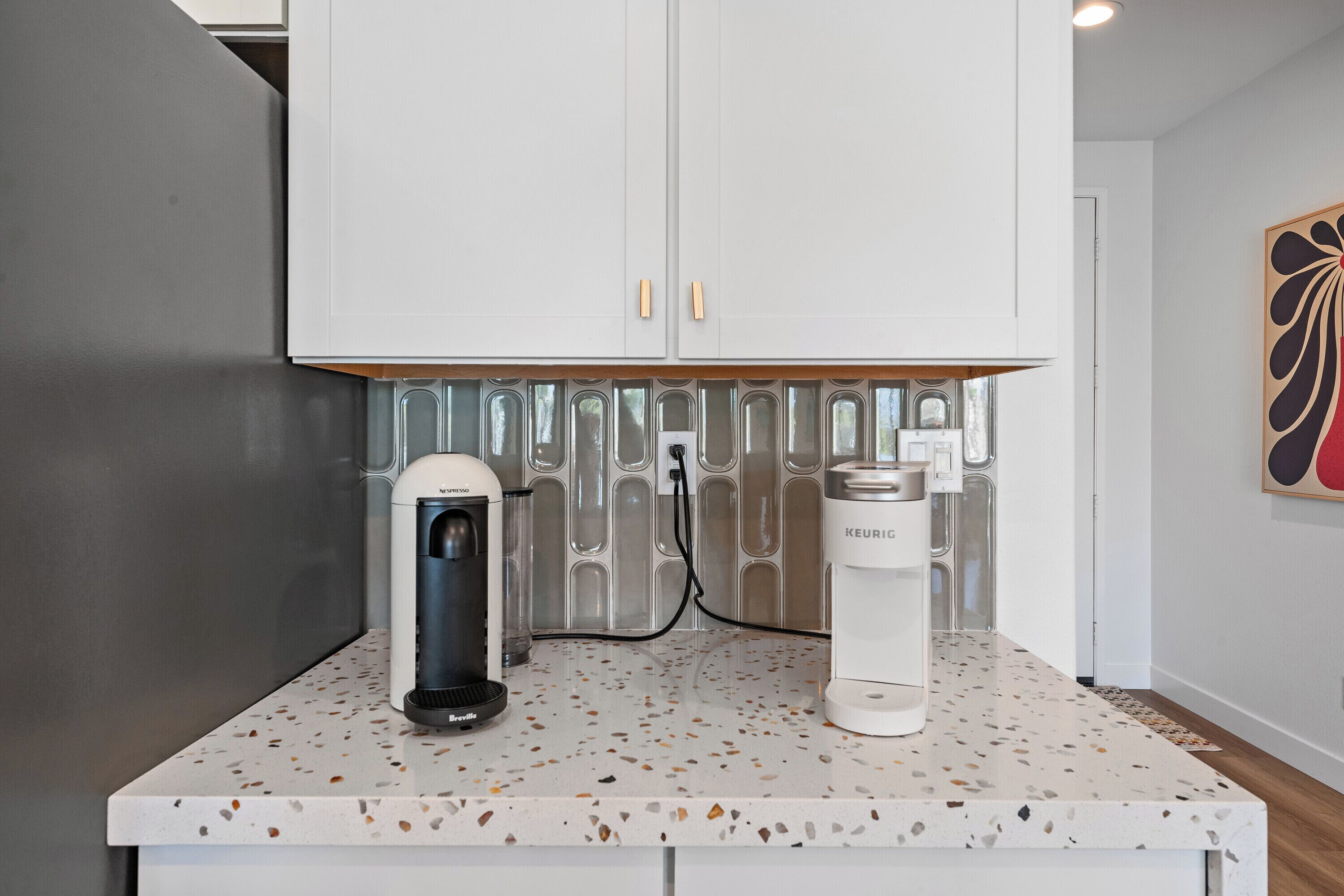 A kitchen with a coffee maker, a water dispenser, and a kettle on a speckled countertop.