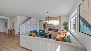 A modern living room with a large sectional sofa, a flat-screen TV, and a staircase with a decorative wall. - Electric Slide- Lazy River, Pickleball, Resort backyard & Game room (coachella)
