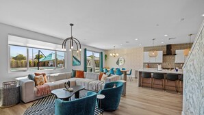 A modern living room with a sectional sofa, a dining area, and a kitchen with bar seating. - Electric Slide- Lazy River, Pickleball, Resort backyard & Game room (coachella)