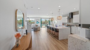 A modern kitchen with a central island, white cabinetry, and a large mirror. - Electric Slide- Lazy River, Pickleball, Resort backyard & Game room (coachella)