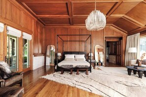 Une chambre spacieuse avec un lit à baldaquin, des boiseries, un lustre et une grande fenêtre.