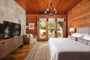 Une chambre avec un plafond en bois, une télévision, un lit avec une literie à rayures, un canapé et une vue sur l’extérieur, visible à travers une porte vitrée.