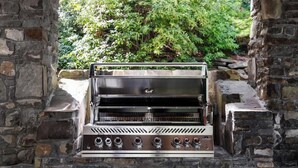 A stone-built outdoor grill with a glass top, surrounded by stone walls and greenery.